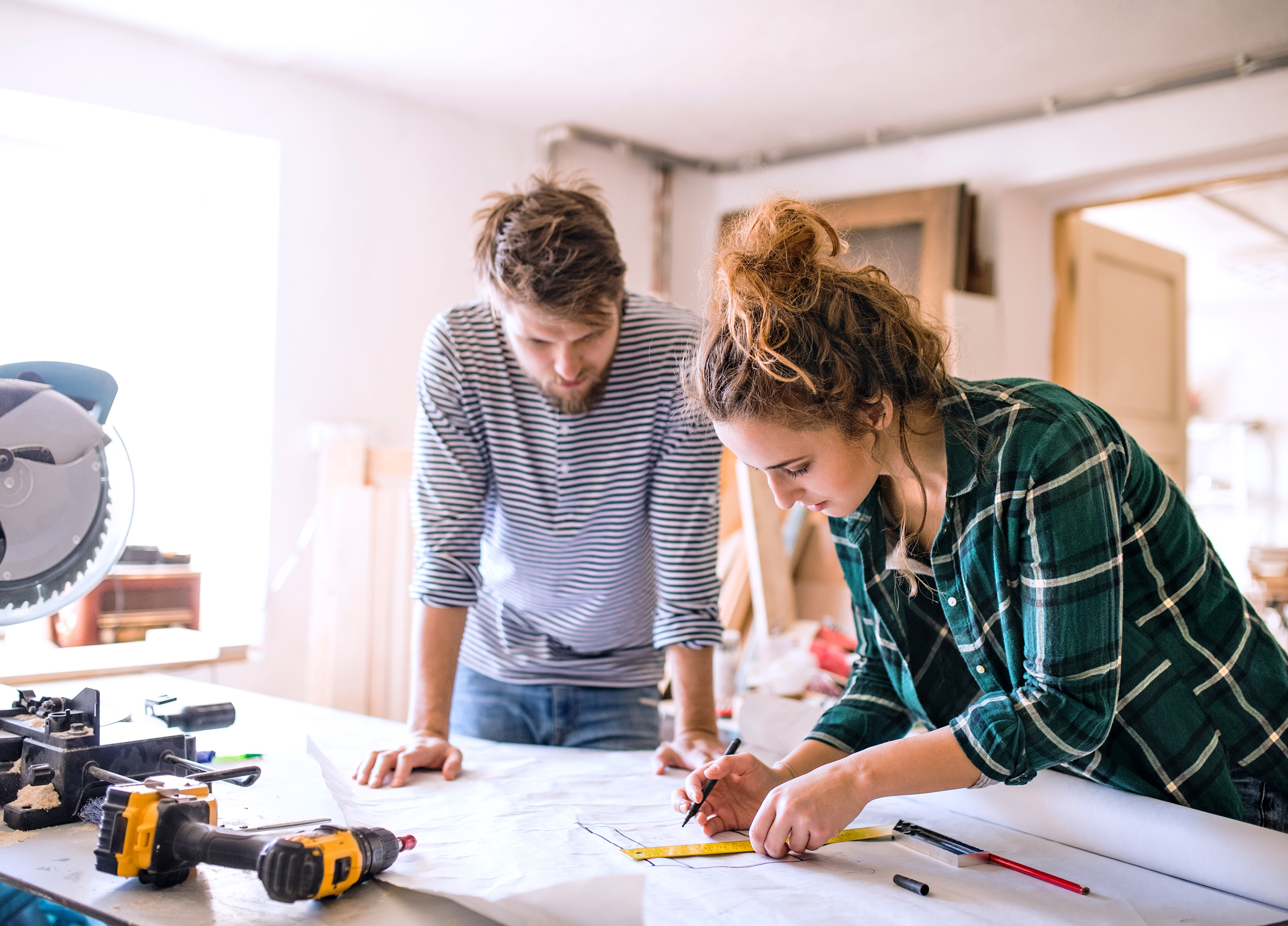 A girl and a guy measuring their drawings in the midst of their renovation